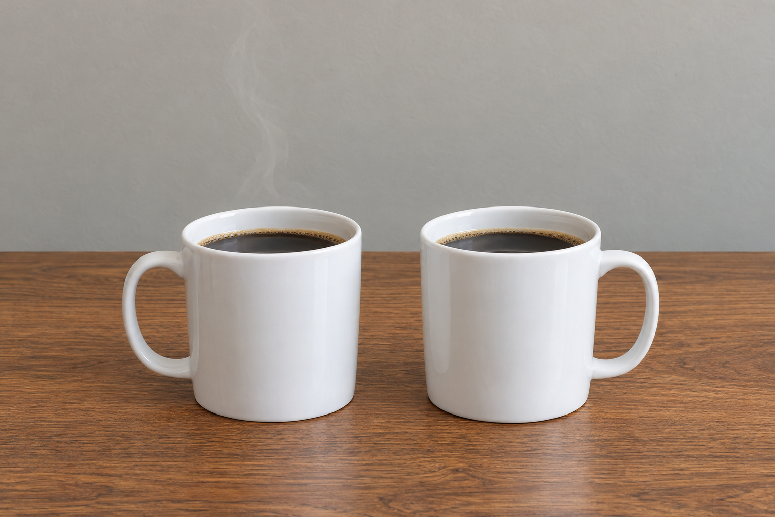Two identical mugs of coffee side by side on an office desk; steam rises from one mug, and the other has no steam.