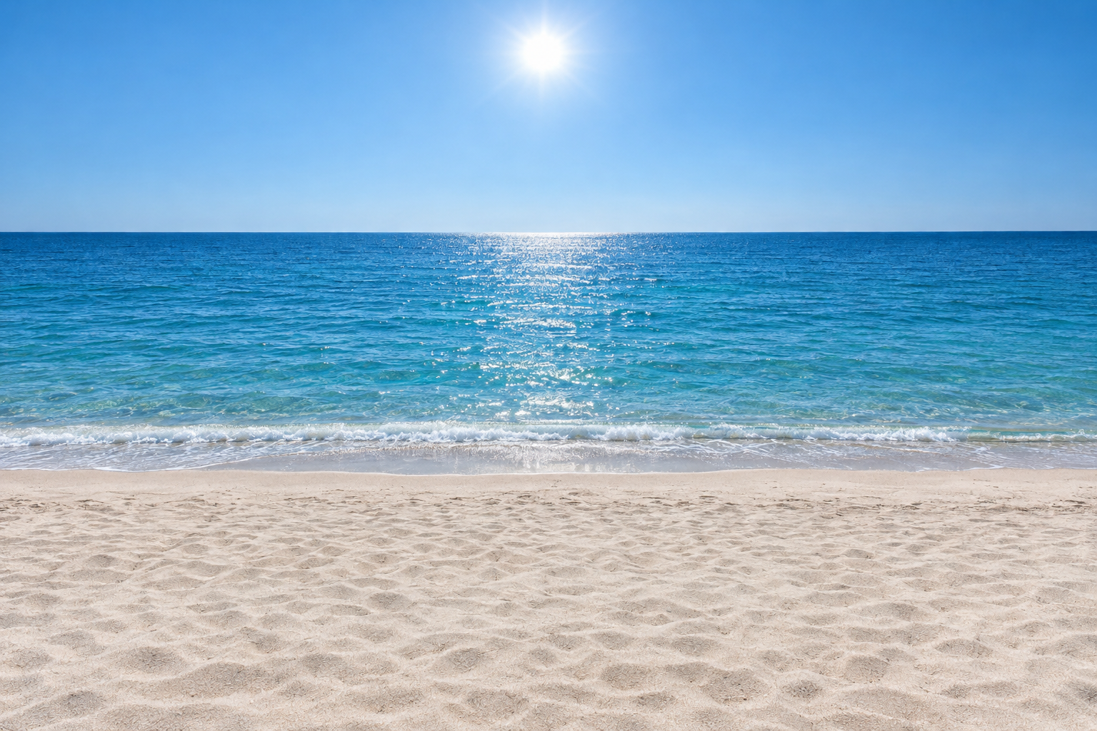 A sunny beach at midday: dry sand in the foreground, calm sea behind it, one sun high in a clear sky.