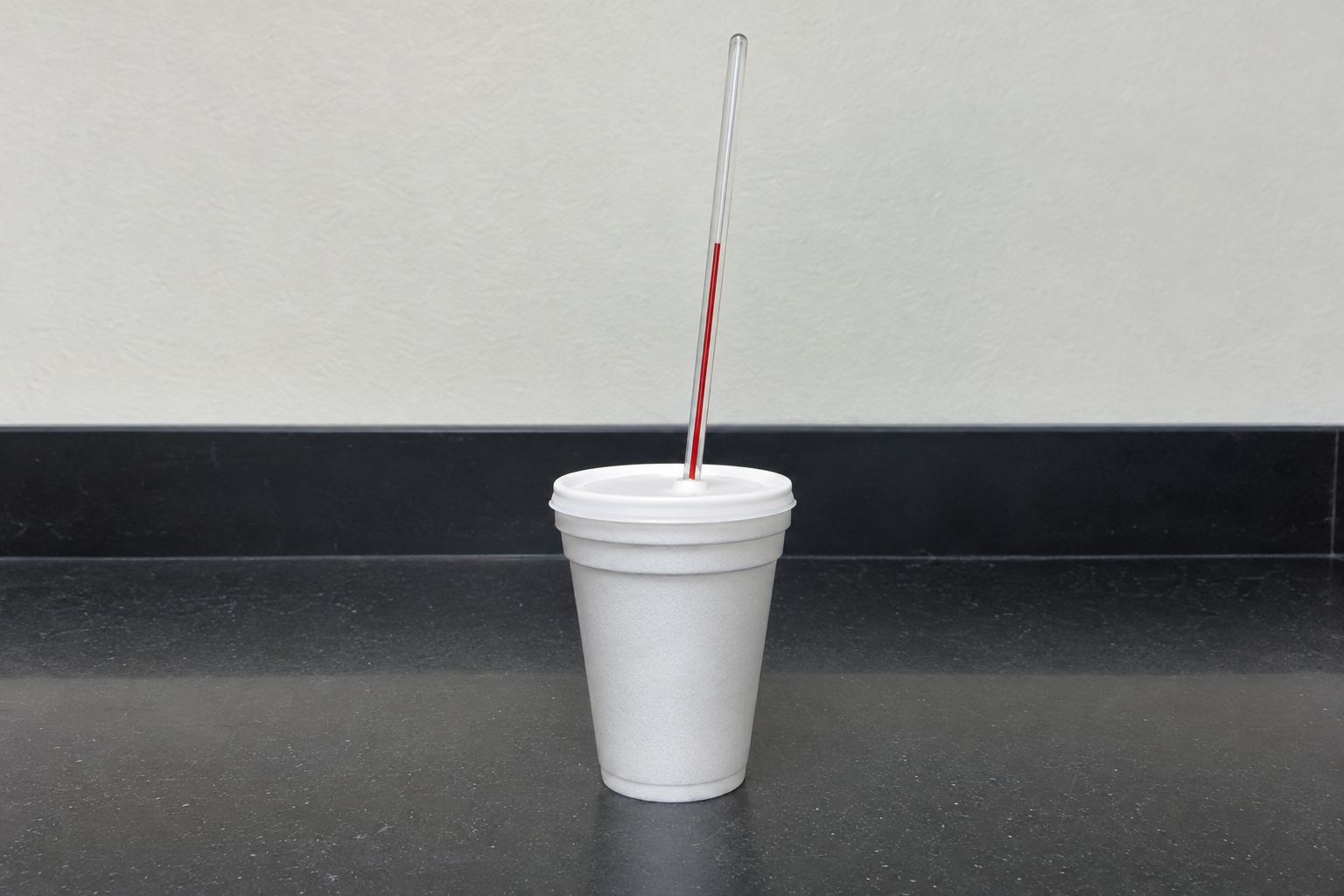 A real coffee-cup calorimeter on a lab bench: two nested white foam cups with a lid, and a glass thermometer standing through a hole in the lid.
