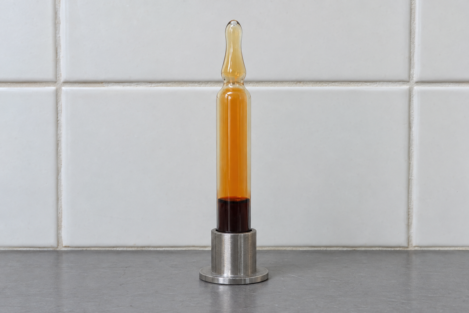 A sealed glass ampoule with dark liquid bromine pooled at the bottom and orange bromine vapor filling the space above it.
